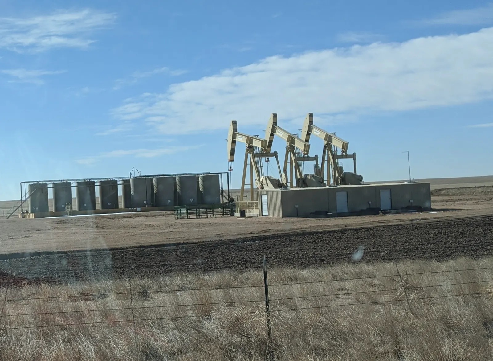 Oil and gas in Colorado: pumpjacks and storage tanks at an oil well site beside Colorado Highway 14 near the Pawnee National Grassland