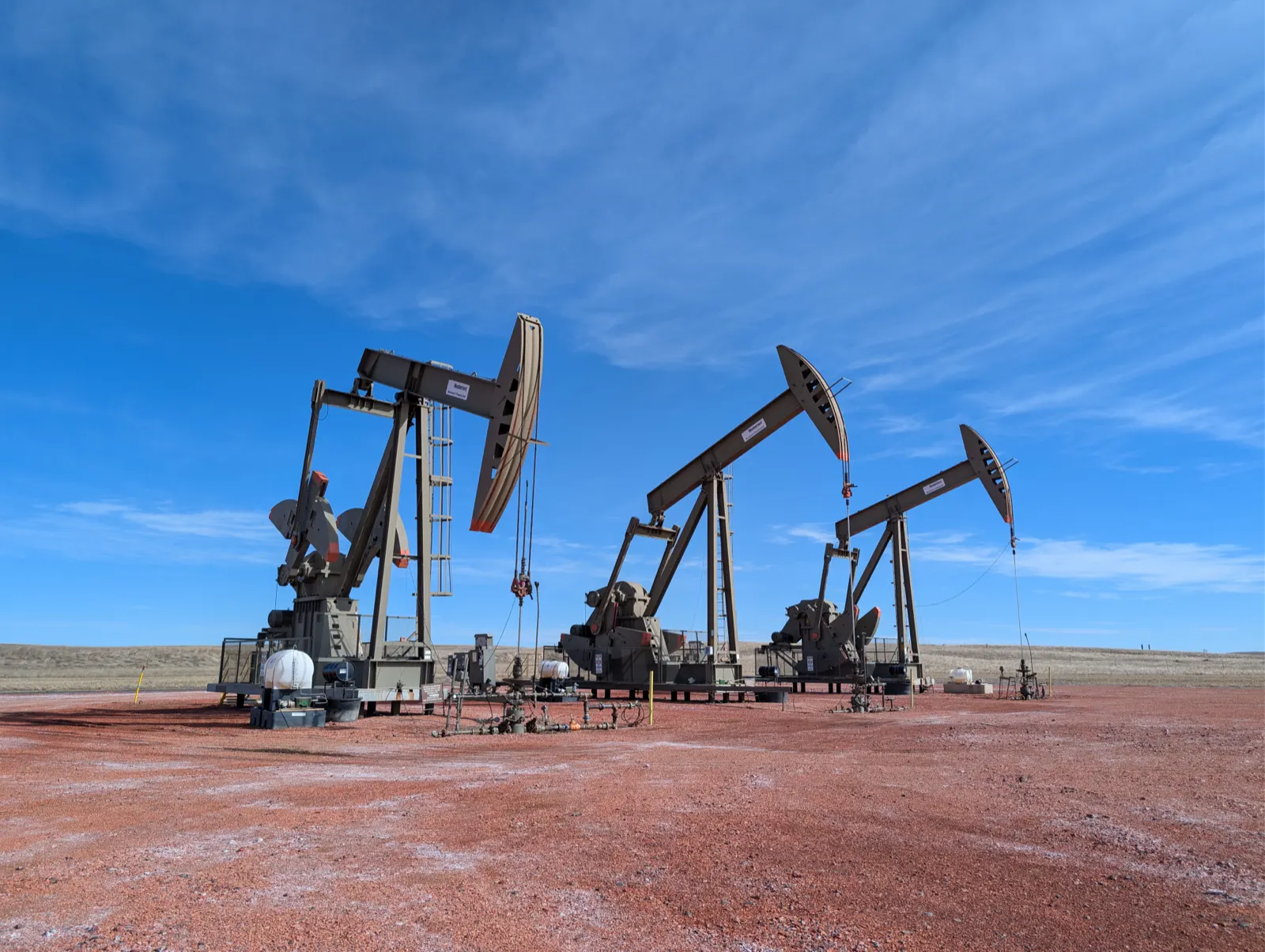 Oil and gas in North Dakota: three pumpjacks on a multi-well oil pad of red scoria rock in the Little Missouri National Grassland, North Dakota