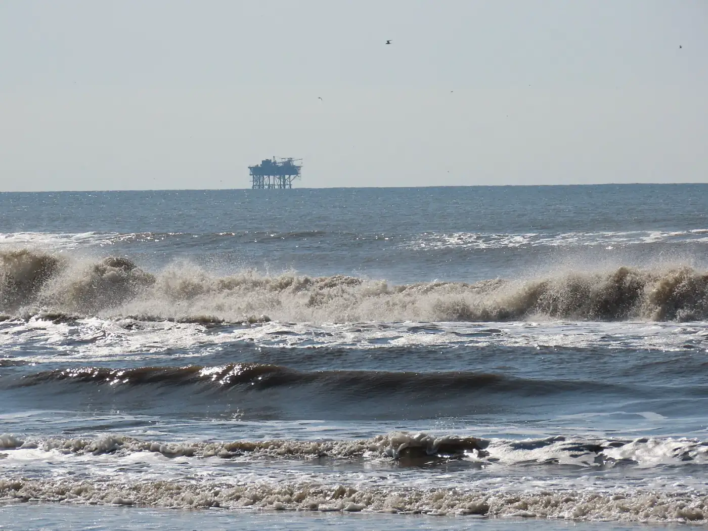 Sell mineral rights in Louisiana: surf breaking on Grand Isle, Louisiana, with an offshore oil platform on the horizon